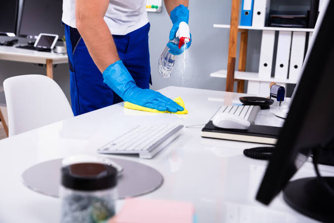 Cleaner wiping down a desk during a scheduled sanitization visit